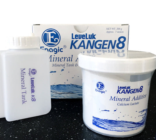 Hvit pakke i bakgrunnen, med blå skrift. Foran pakken står hvit plastflaske med hvit skrukork og blå skrift. Ved siden av står hvit boks med hvit skrukork og blå skrift. Produktene står på et mørkeblått bord.