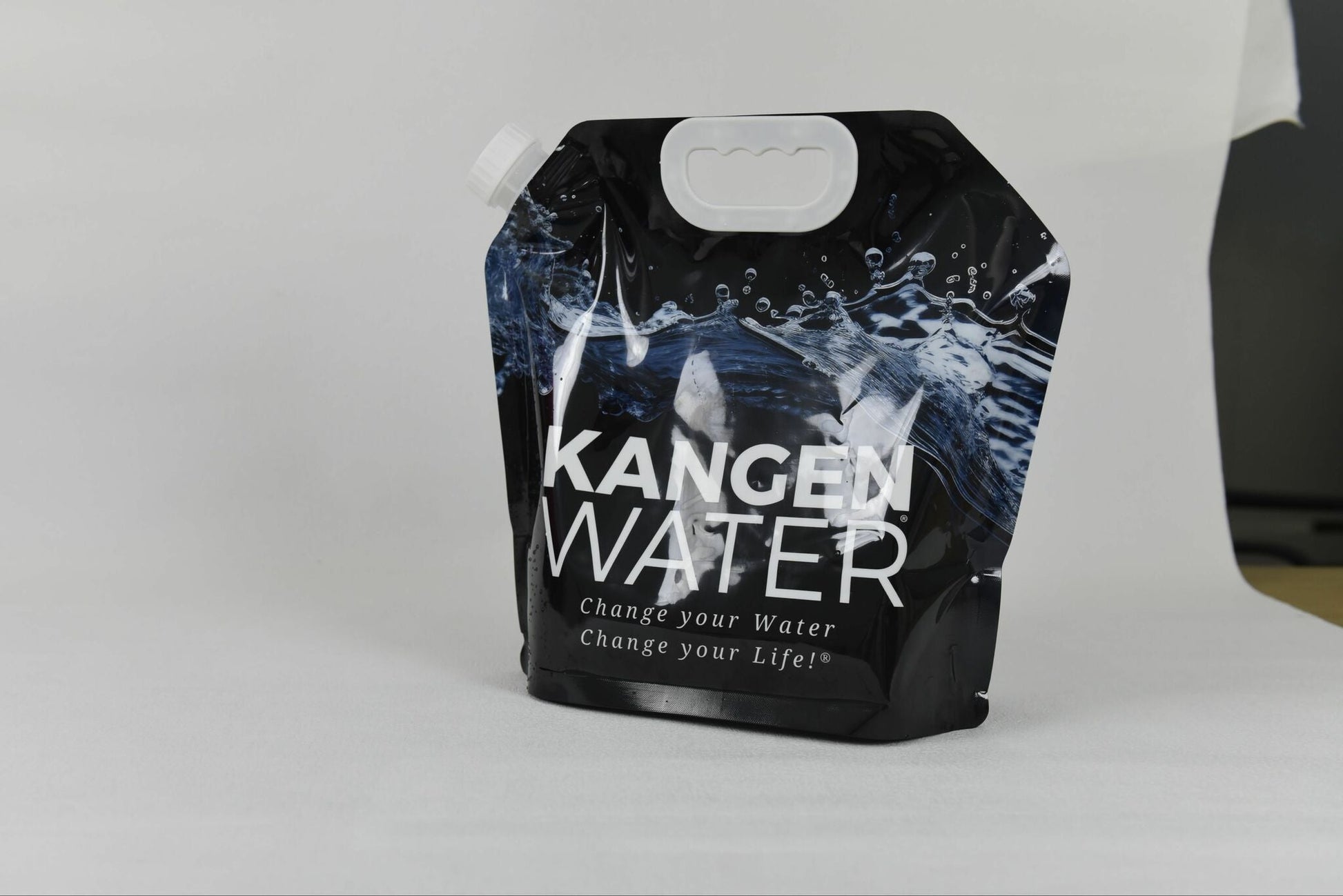 Mørk plastpose til vann, med hvit logo på framsiden. Posen har detaljer av bølgende vann. Hvit bakgrunn.